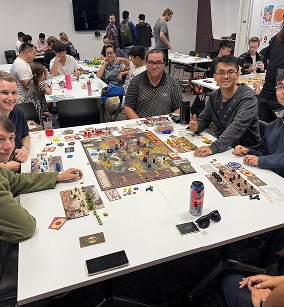 Vrienden verzamelden zich rond een tafel om een complex bordspel te spelen tijdens een clubavond.